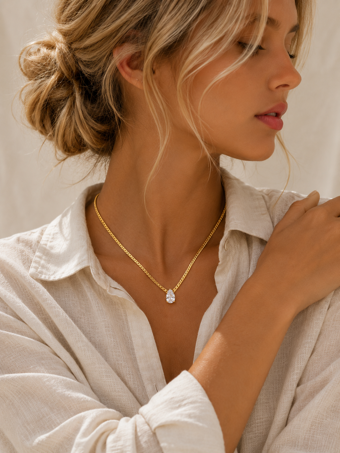 Woman wearing the Adeline Gold Necklace with a brilliant pear-cut white zircon pendant by Maison Élyséa